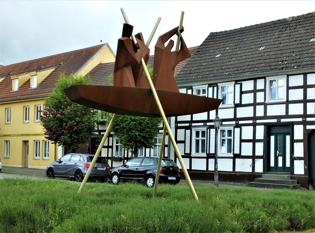 Die kunstvolle Skulptur „Fluss-Schiffer“ von Witte-Kropius in schöner Stadtkulisse.
